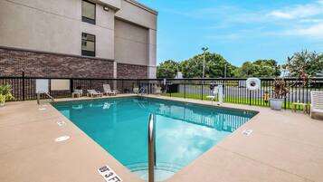 A rectangular indoor pool with a metal safety railing, surrounded by a black fence.