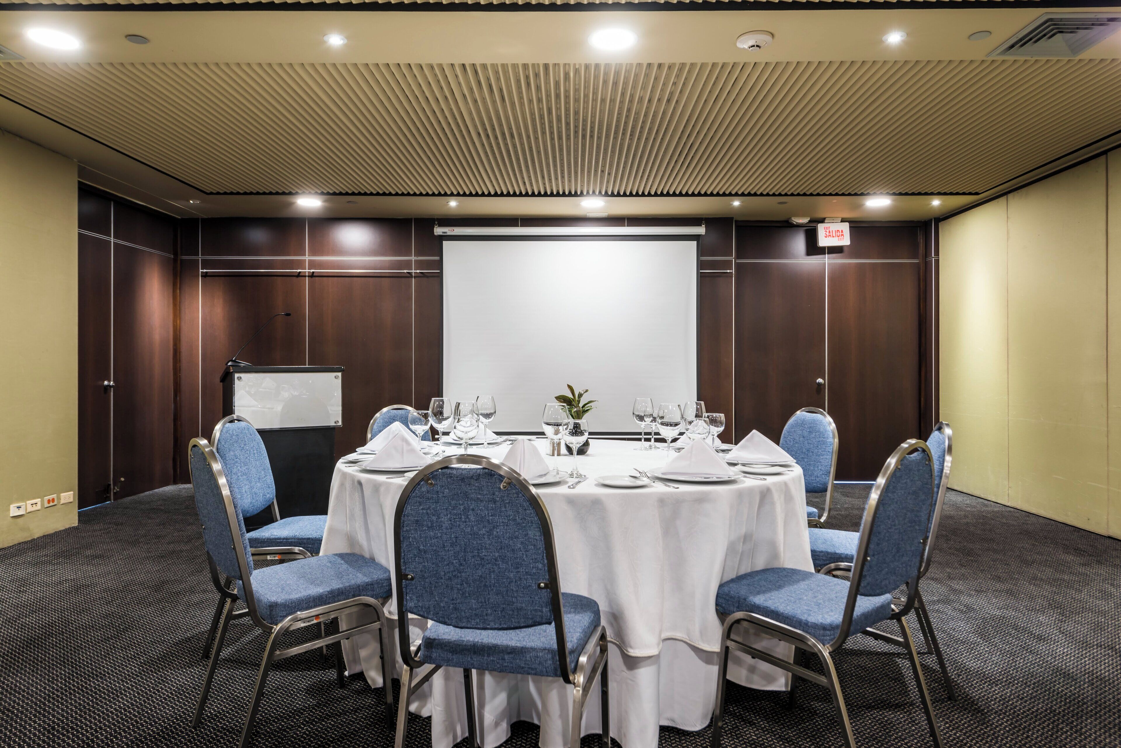 A conference room with a white table, blue chairs, and a projector screen.