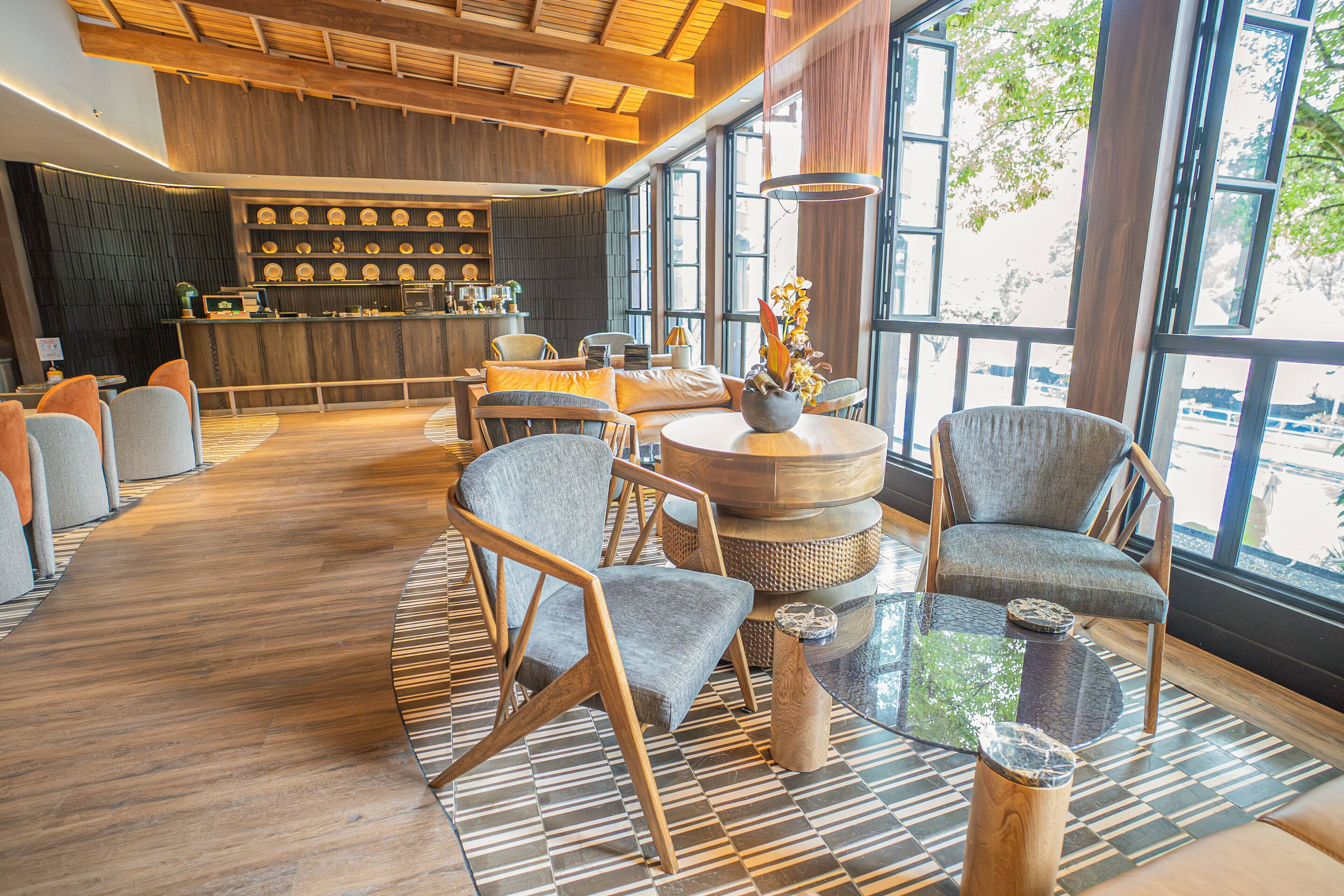 A modern interior with a wooden reception desk, seating area with round tables, and large windows offering views.