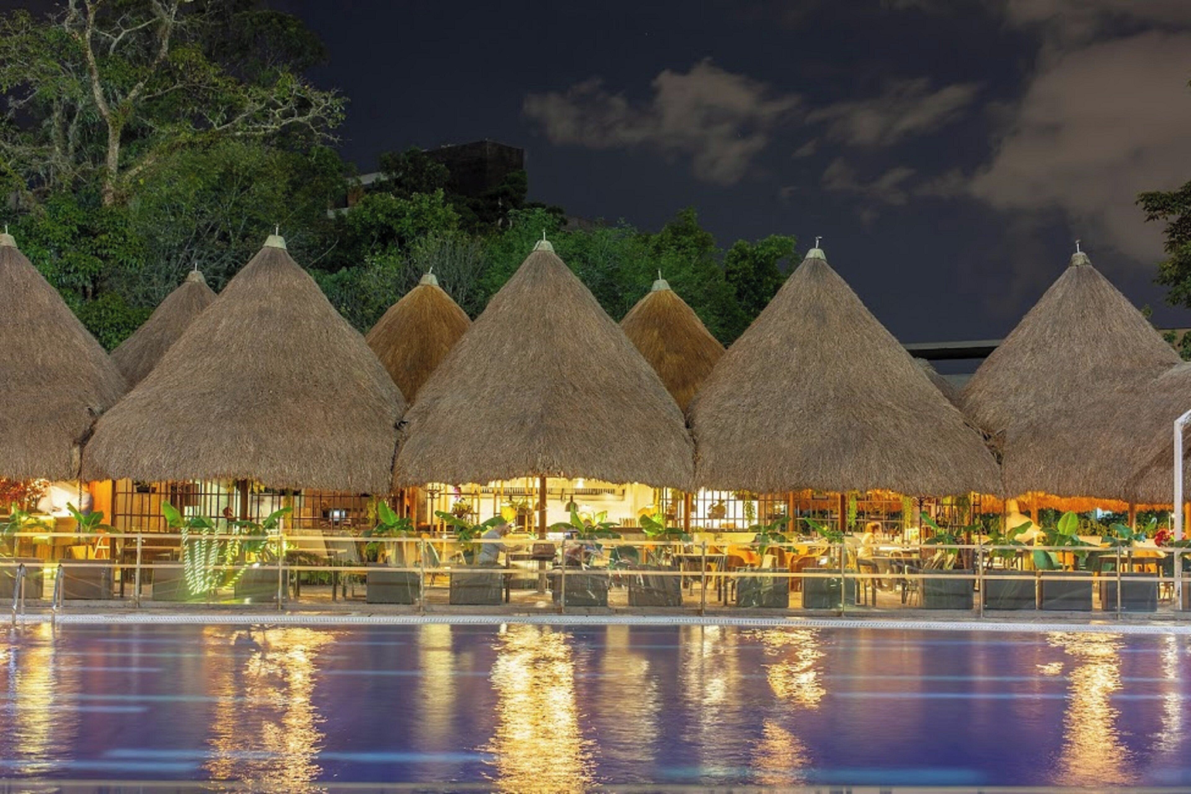 A series of thatched-roof structures with a pool in the foreground.
