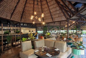 A restaurant with a thatched roof, cushioned seating, and a variety of plants. - InterContinental Medellin - Movich by IHG (Medellín)