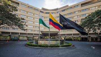 A hotel entrance with a large building, multiple flags, and a fountain.