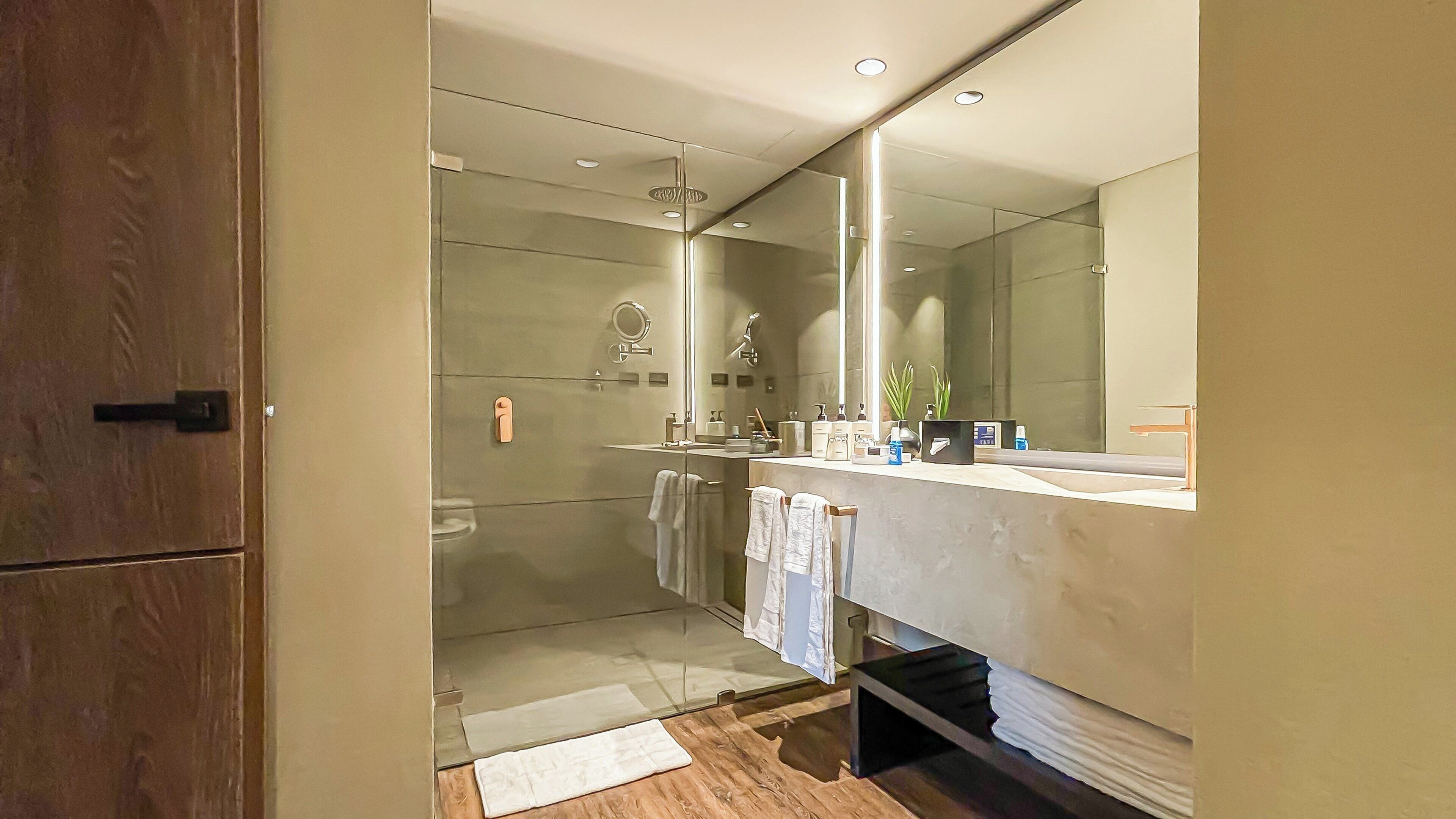 A modern bathroom with a large mirror, a shower, and a vanity with a sink and towel rack.