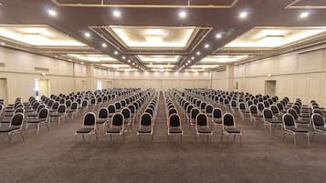 A large conference room with rows of chairs, a carpeted floor, and a high ceiling with recessed lighting.