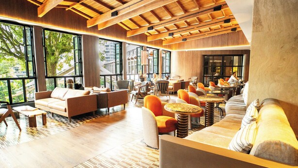 A modern interior with large windows, wooden ceiling beams, and a mix of seating arrangements including sofas and round tables. - InterContinental Medellin - Movich by IHG (Medellín)
