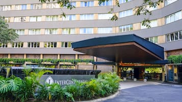 A multi-story hotel with a modern facade, a covered entrance, and a landscaped area with a water feature.