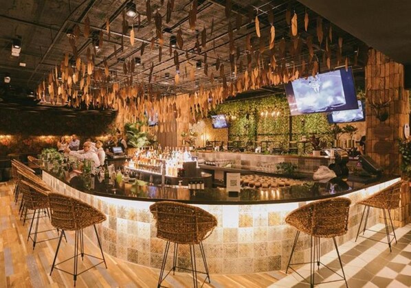 A bar area with a curved counter, wicker bar stools, and hanging wooden elements. - InterContinental Medellin - Movich by IHG (Medellín)