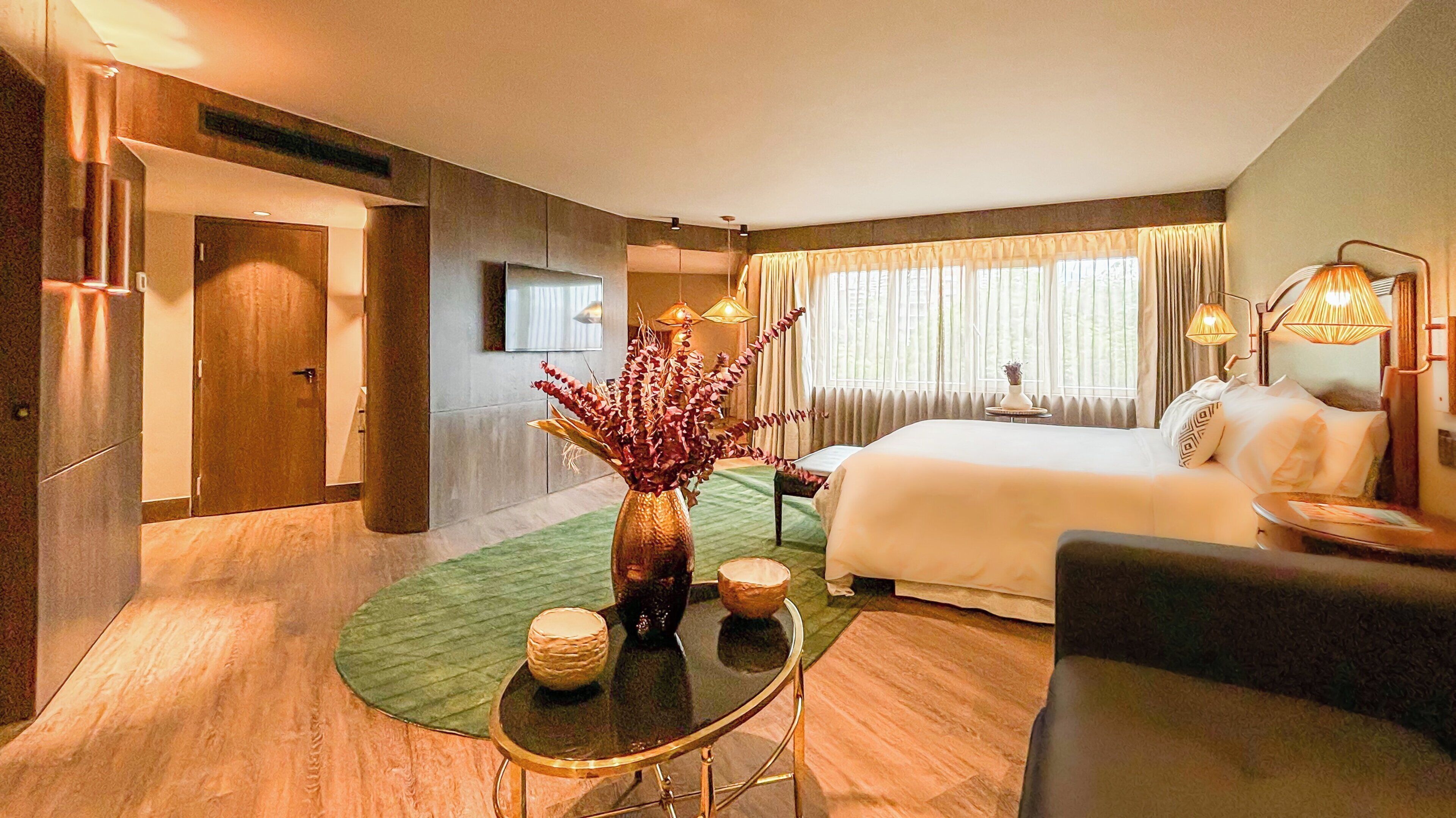 A hotel room with a bed, a sitting area with a table and chairs, a vase with flowers, and a television on the wall.