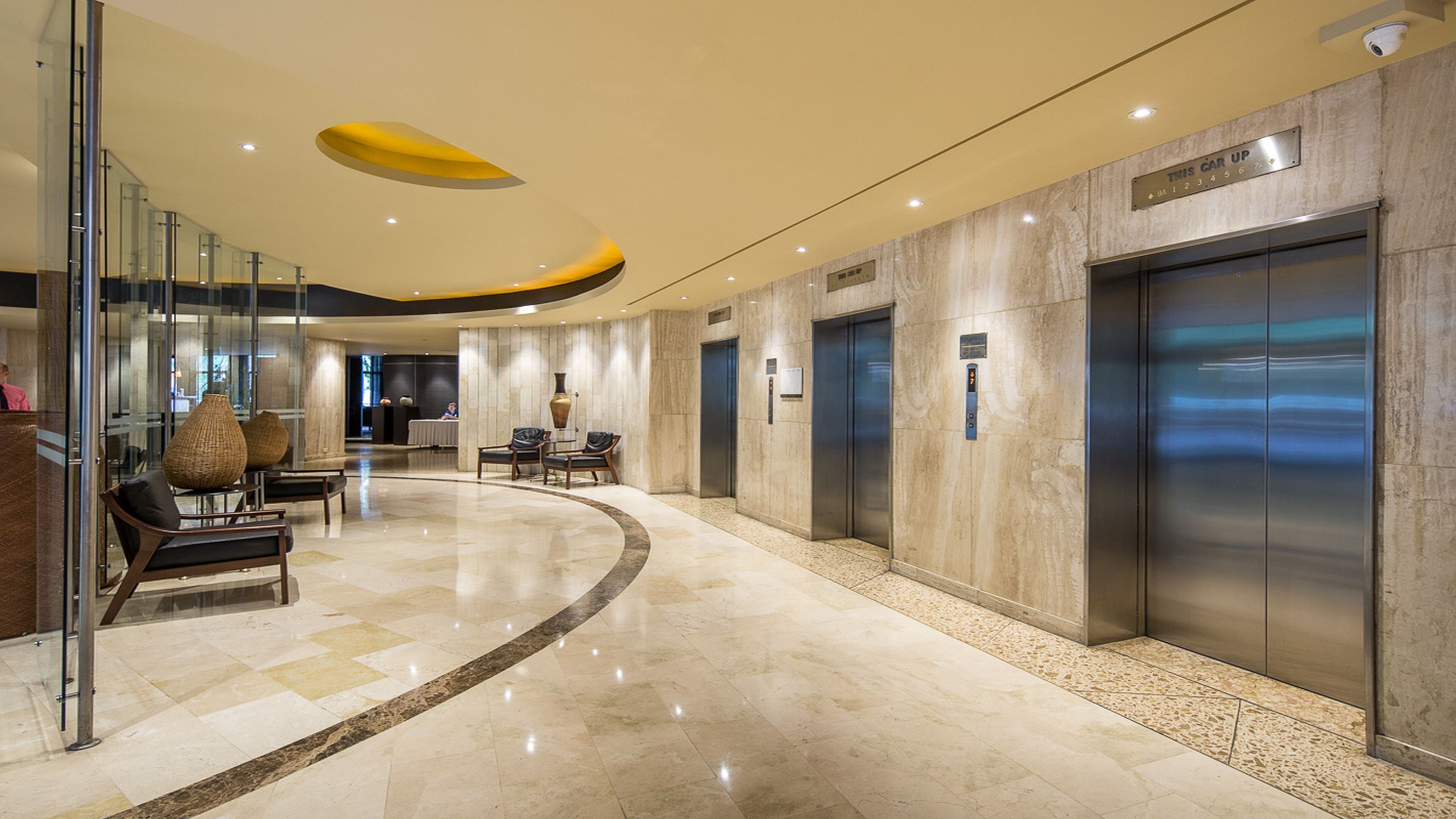 A modern lobby with a curved floor, glass walls, and a seating area with chairs and tables.
