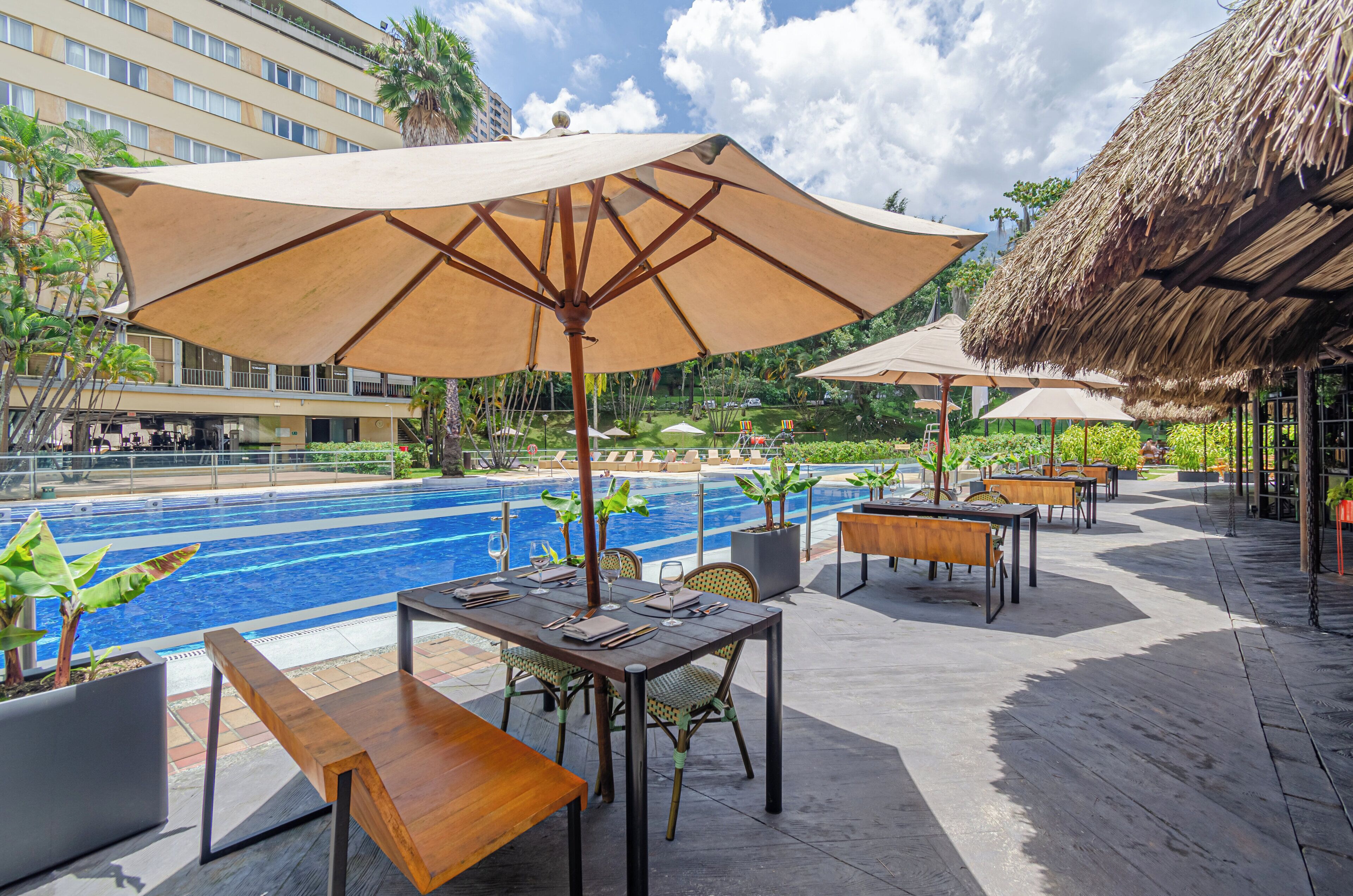 A poolside area with tables and chairs, umbrellas, and a pool.