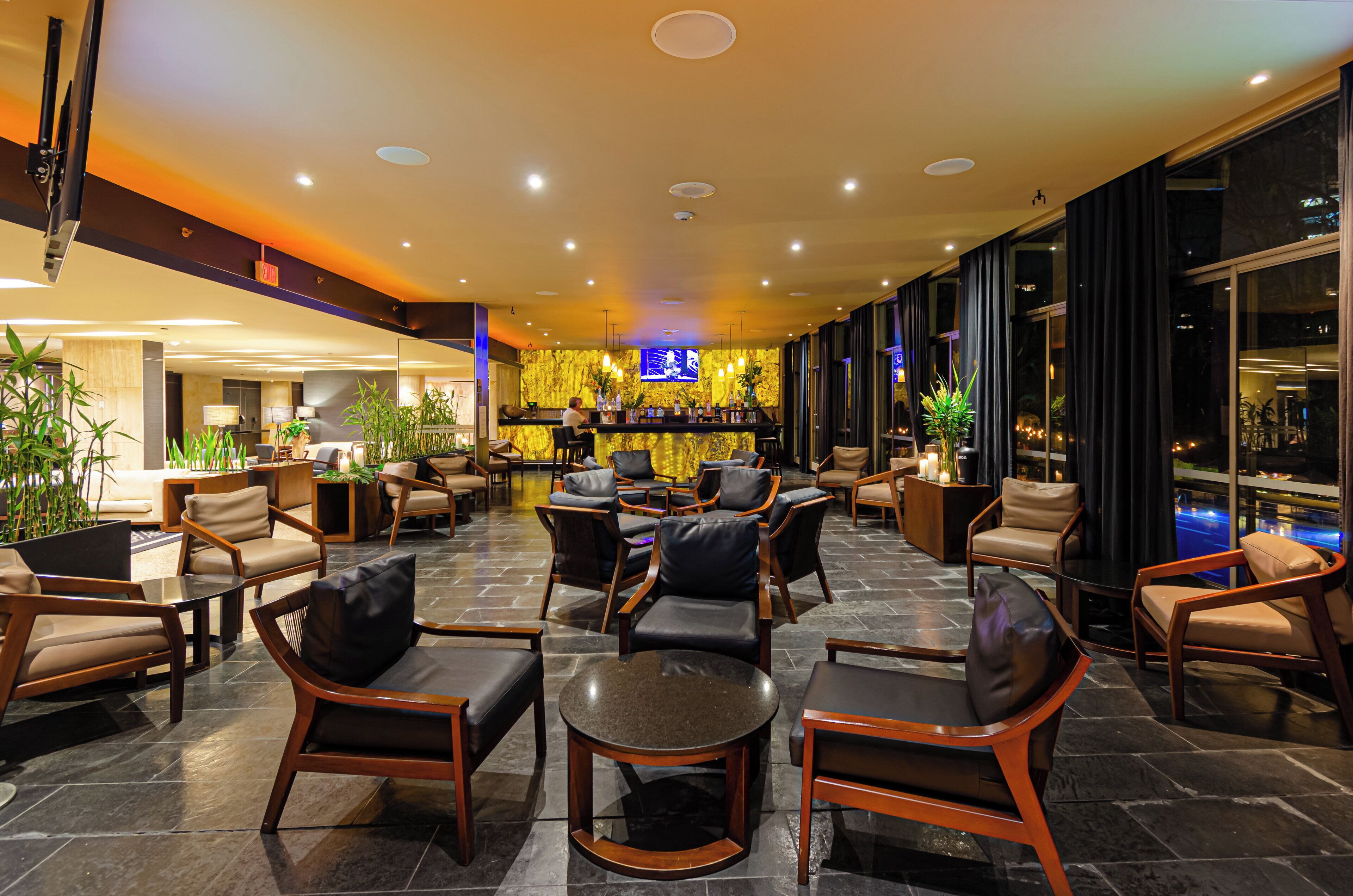 A spacious lobby with leather chairs, a bar area, and large windows offering a view of the cityscape.