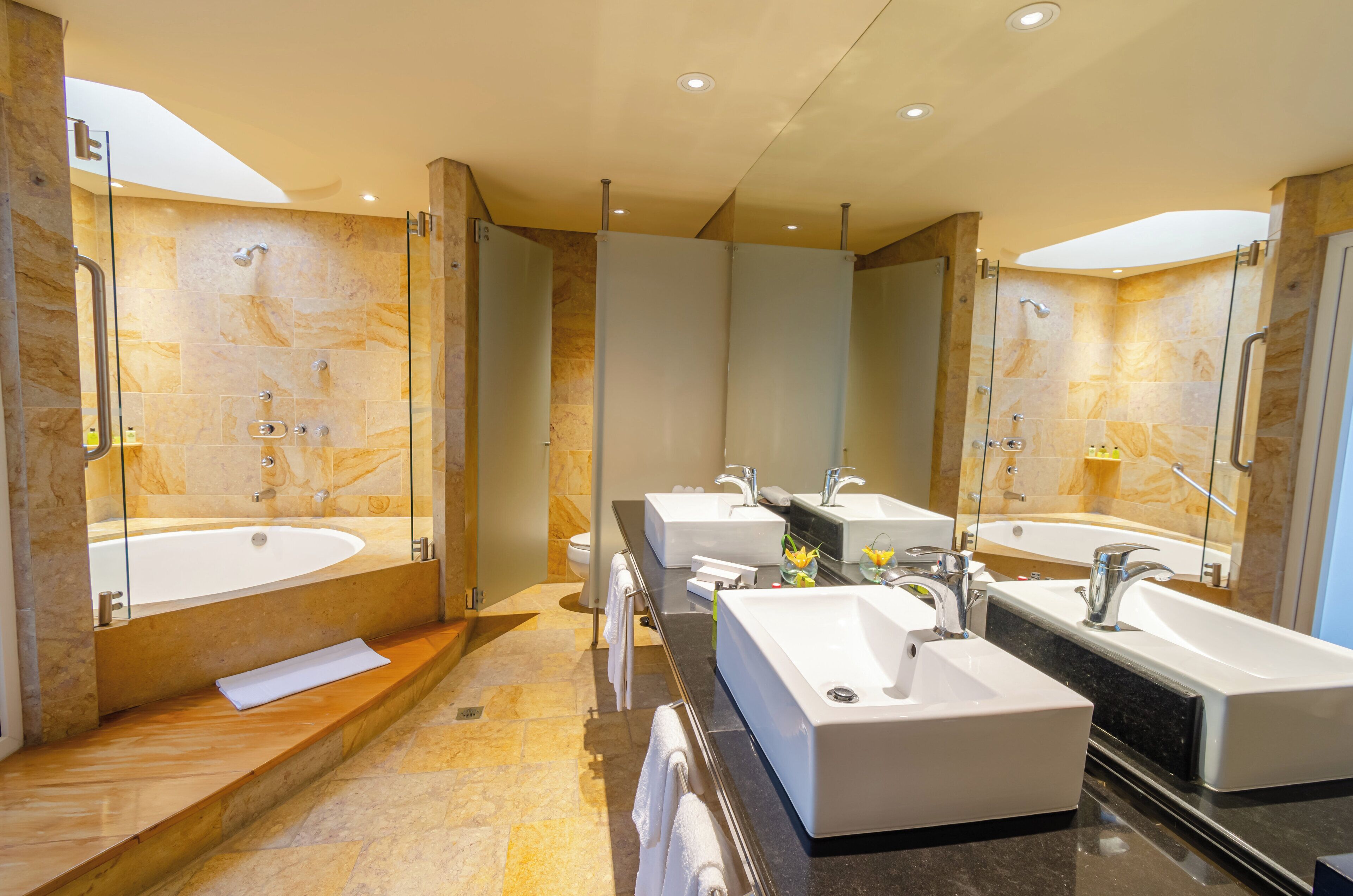 A modern bathroom with a large bathtub, two sinks, and a glass shower enclosure.