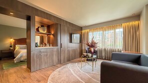 A modern hotel room with a wooden floor, a sofa, a TV, and a dining area with a table and chairs.