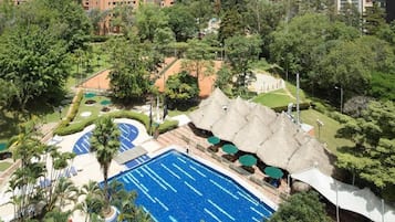 A swimming pool surrounded by lush greenery, a thatched-roof structure, and a well-maintained garden area.