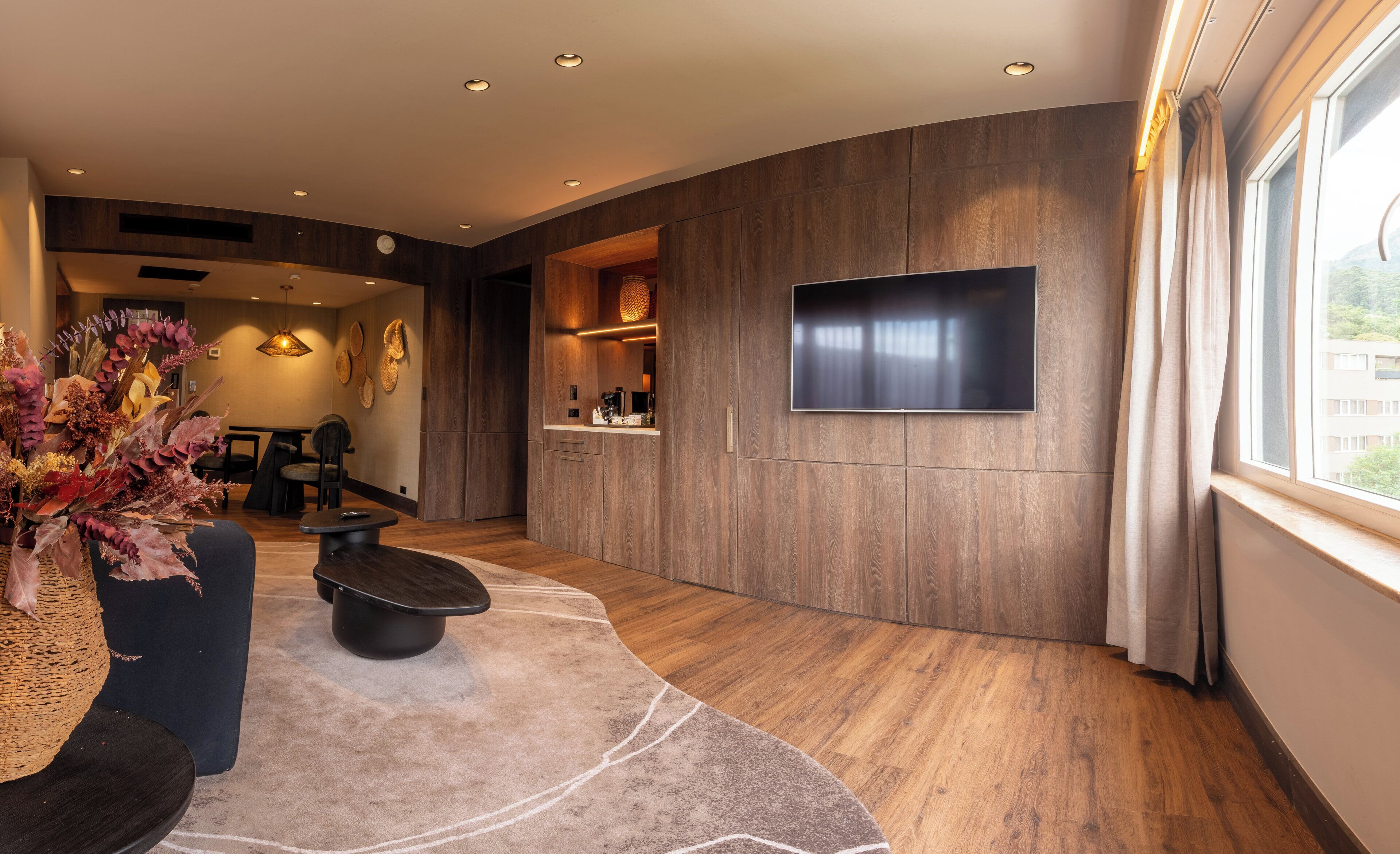 Una sala de estar moderna con un televisor de pantalla plana montado en la pared, un comedor con sillas y una cocina con mostrador y electrodomésticos.
