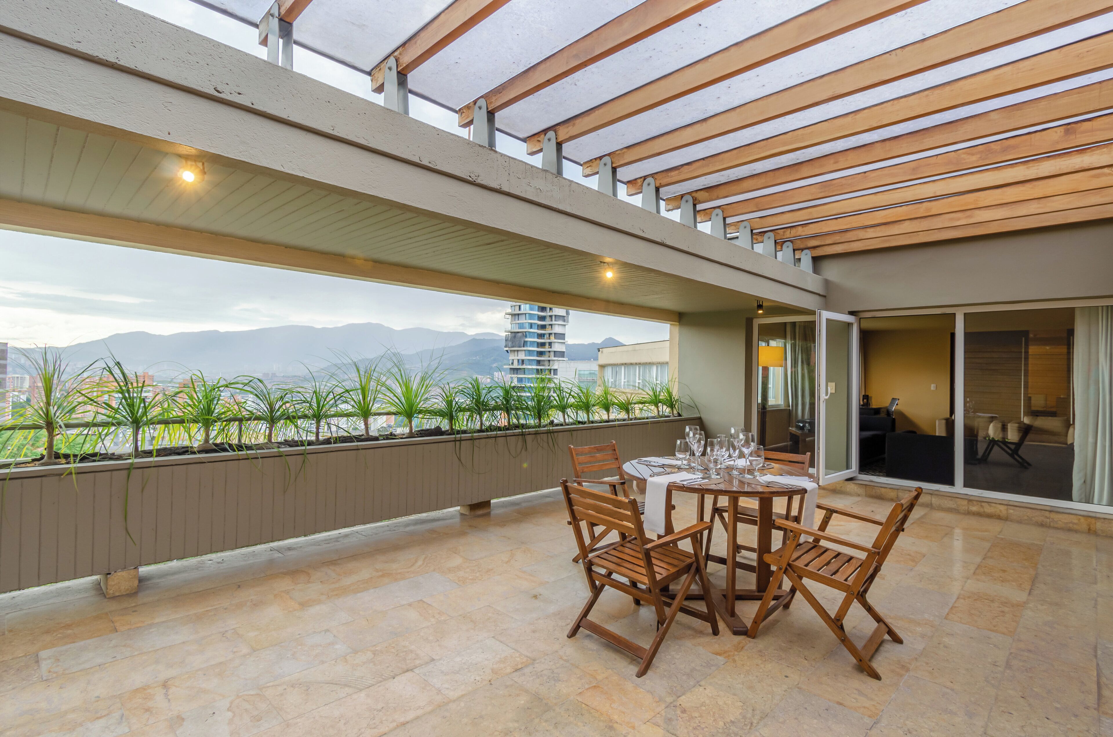 Une vaste terrasse extérieure dotée d’une table et de chaises, d’une pergola au-dessus et offrant une vue sur les montagnes et les bâtiments.