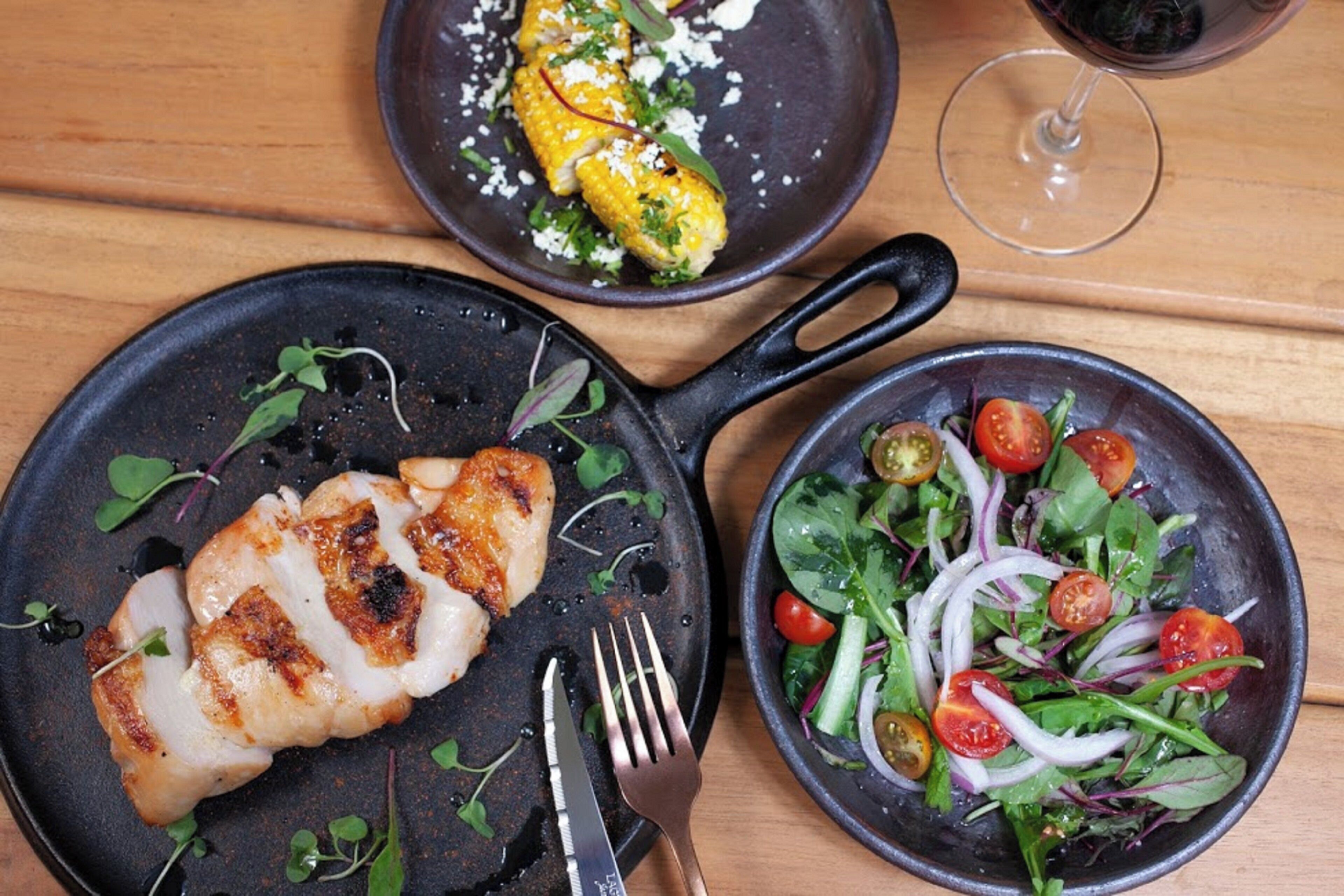 A meal with grilled chicken, corn, and a salad on a wooden table.