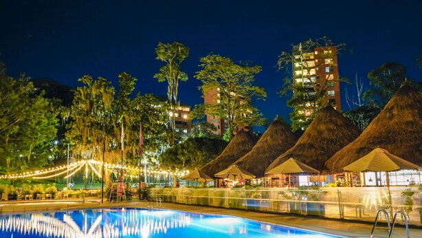 A swimming pool with a thatched-roof structure and string lights in the background. - InterContinental Medellin - Movich by IHG (Medellín)