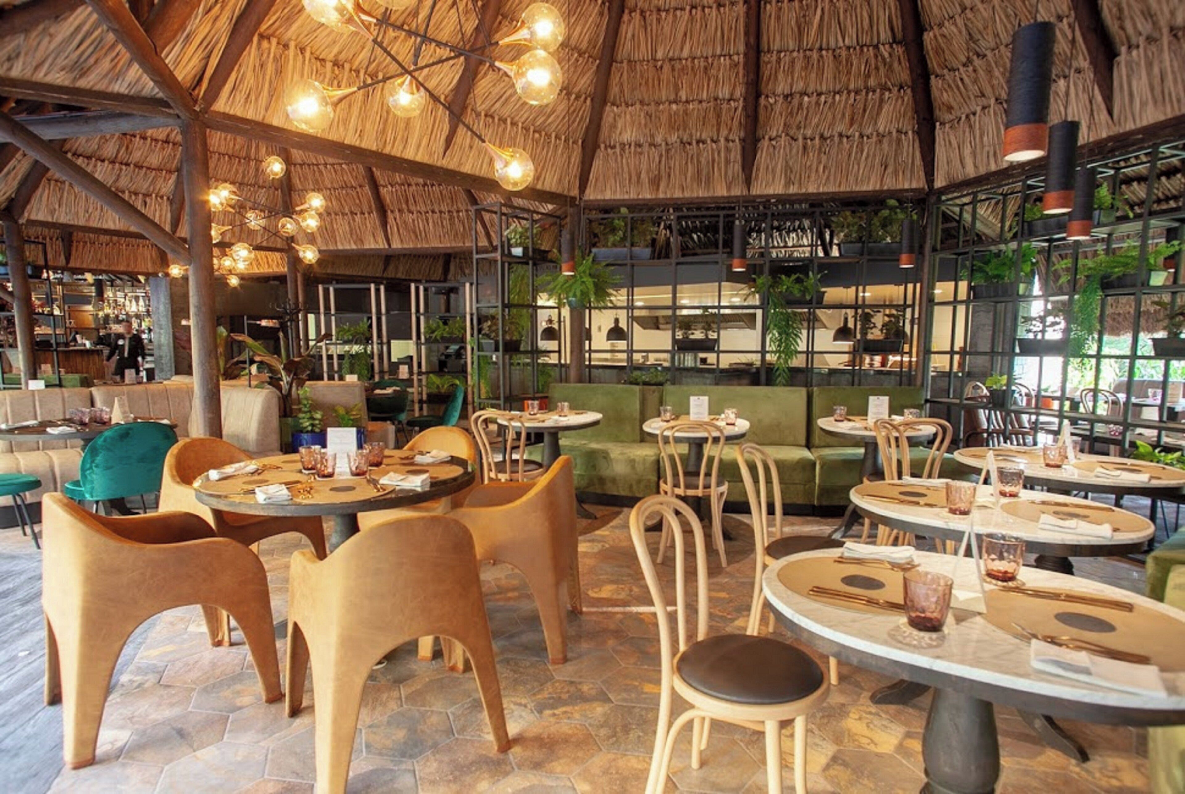 An indoor dining area with round tables, chairs, and a thatched roof ceiling.