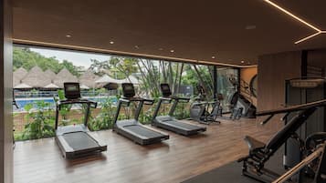 Une salle de sport équipée de tapis de course, de vélos d’exercice et offrant une vue sur une piscine et des arbres.