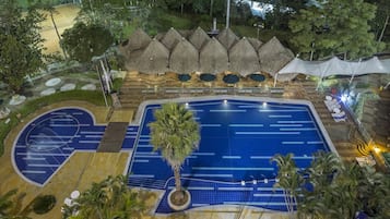 Una piscina con una palmera, rodeada de sombrillas de paja y sillas de descanso.