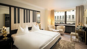 A hotel room with a large bed, a chair, a small table, a desk, and a view of the city. - elaya hotel vienna city center, Trademark by Wyndham (Vienna)
