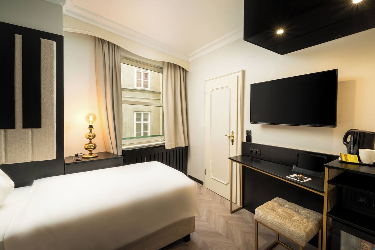 Ein Hotelzimmer mit Bett, Schreibtisch, Stuhl, Fernseher und einem Fenster mit Vorhängen.