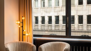Una habitación con dos sillones tapizados, una lámpara de pared y una ventana con vista a un edificio.