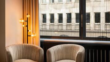 A room with two upholstered chairs, a floor lamp with three light bulbs, and a window with a view of a building.
