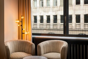 A room with two upholstered chairs, a floor lamp with three light bulbs, and a window with a view of a building. - elaya hotel vienna city center, Trademark by Wyndham (Vienna)