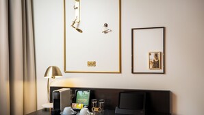 A hotel room with a desk, a lamp, a television, a framed number, and a framed picture on the wall. - elaya hotel vienna city center, Trademark by Wyndham (Vienna)