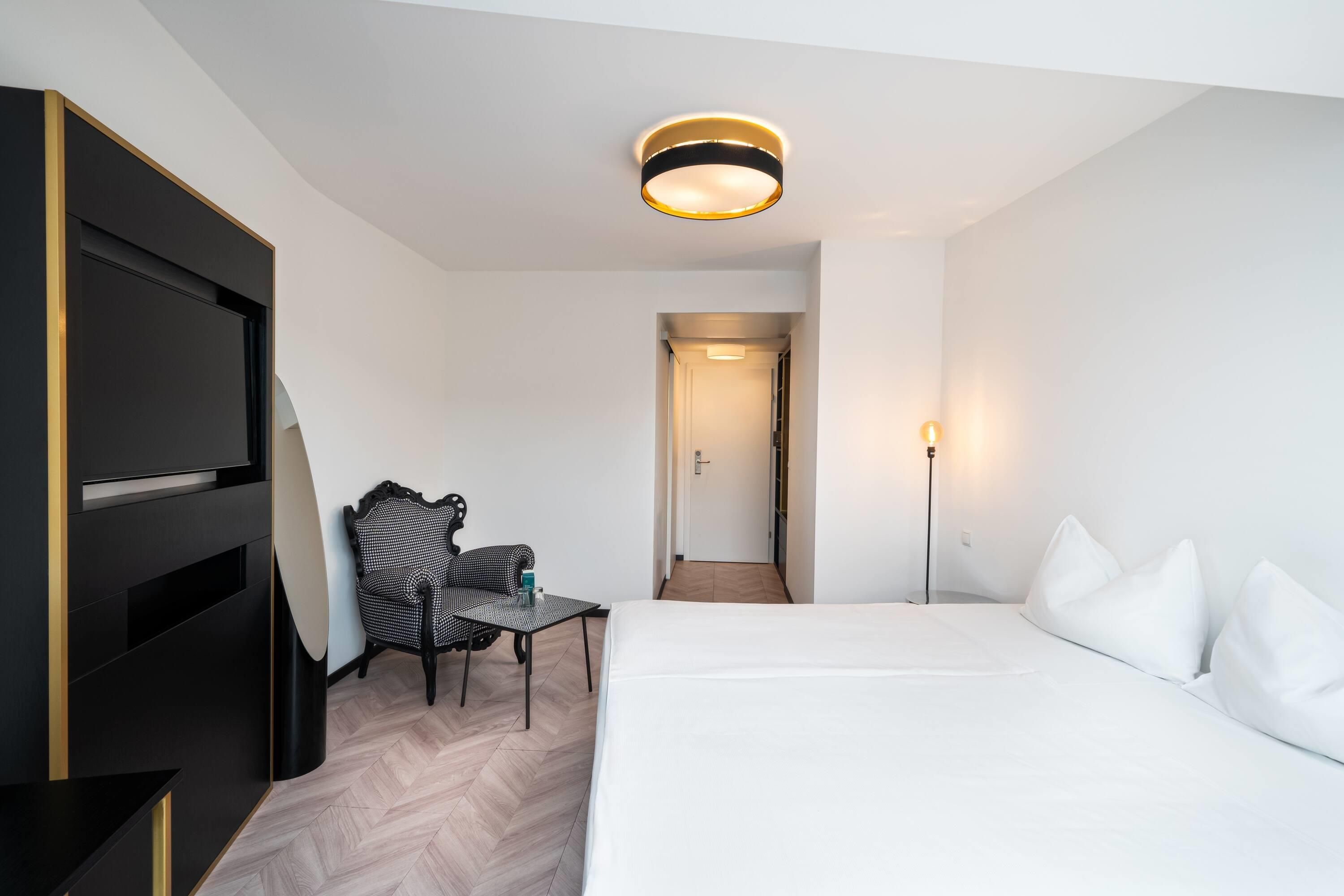Una habitación de hotel con cama, una silla, un escritorio y un televisor.