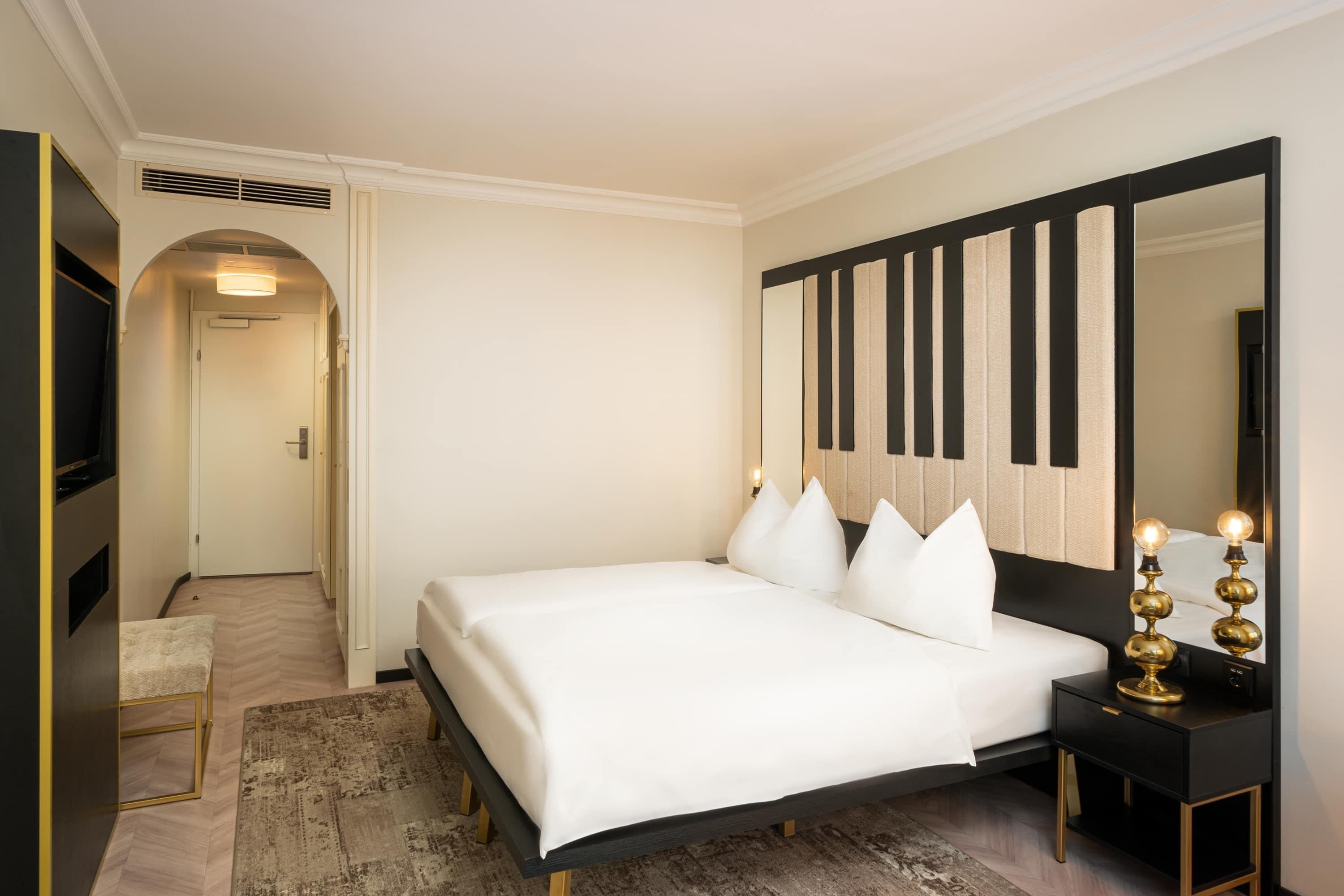 Une chambre d’hôtel avec un lit, un grand miroir, une table de chevet avec une lampe et un sol recouvert de moquette.