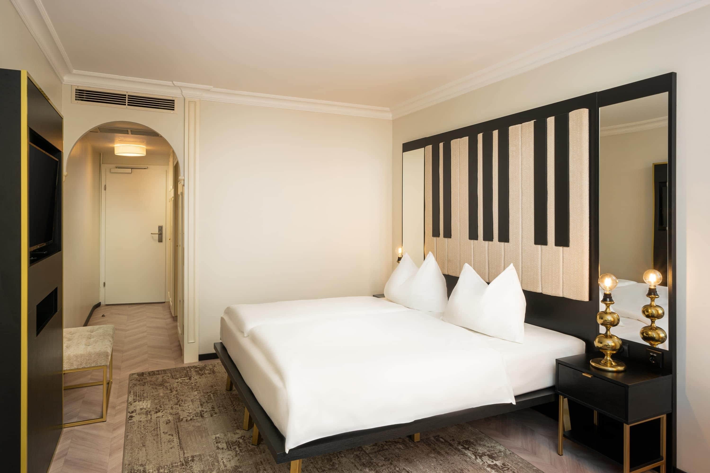 Ein Hotelzimmer mit Bett, einem großen Spiegel, einem Nachttisch mit Lampe und Teppichboden.