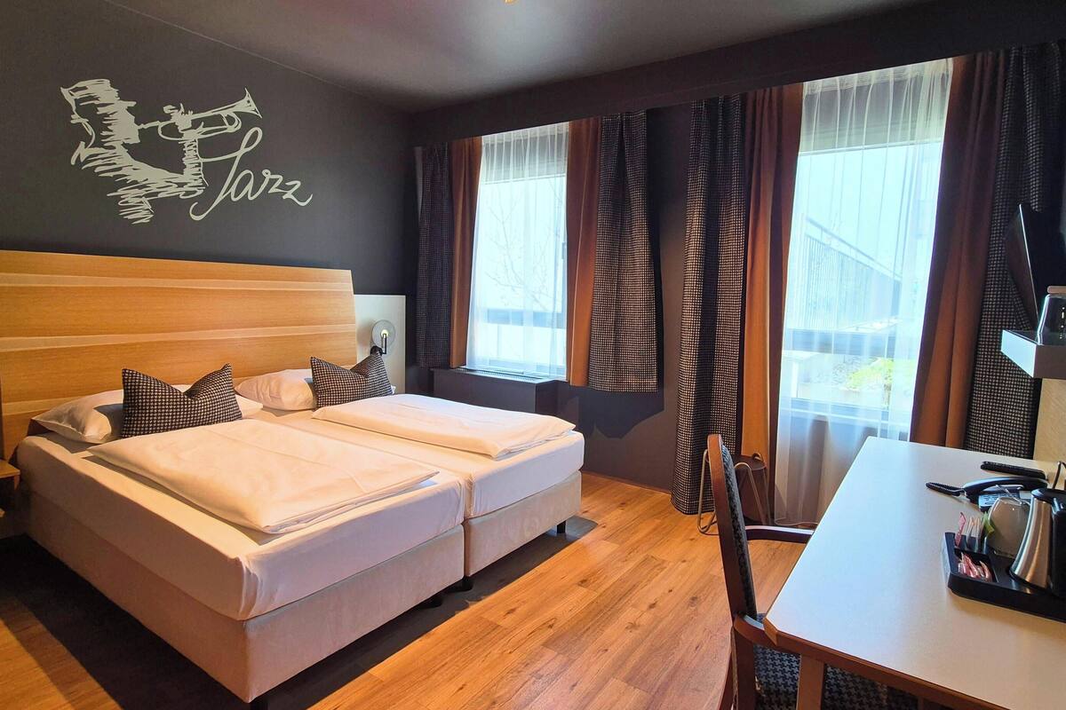 Une chambre d’hôtel avec un lit double, un bureau avec une chaise, une fenêtre avec des rideaux et une œuvre d’art murale.