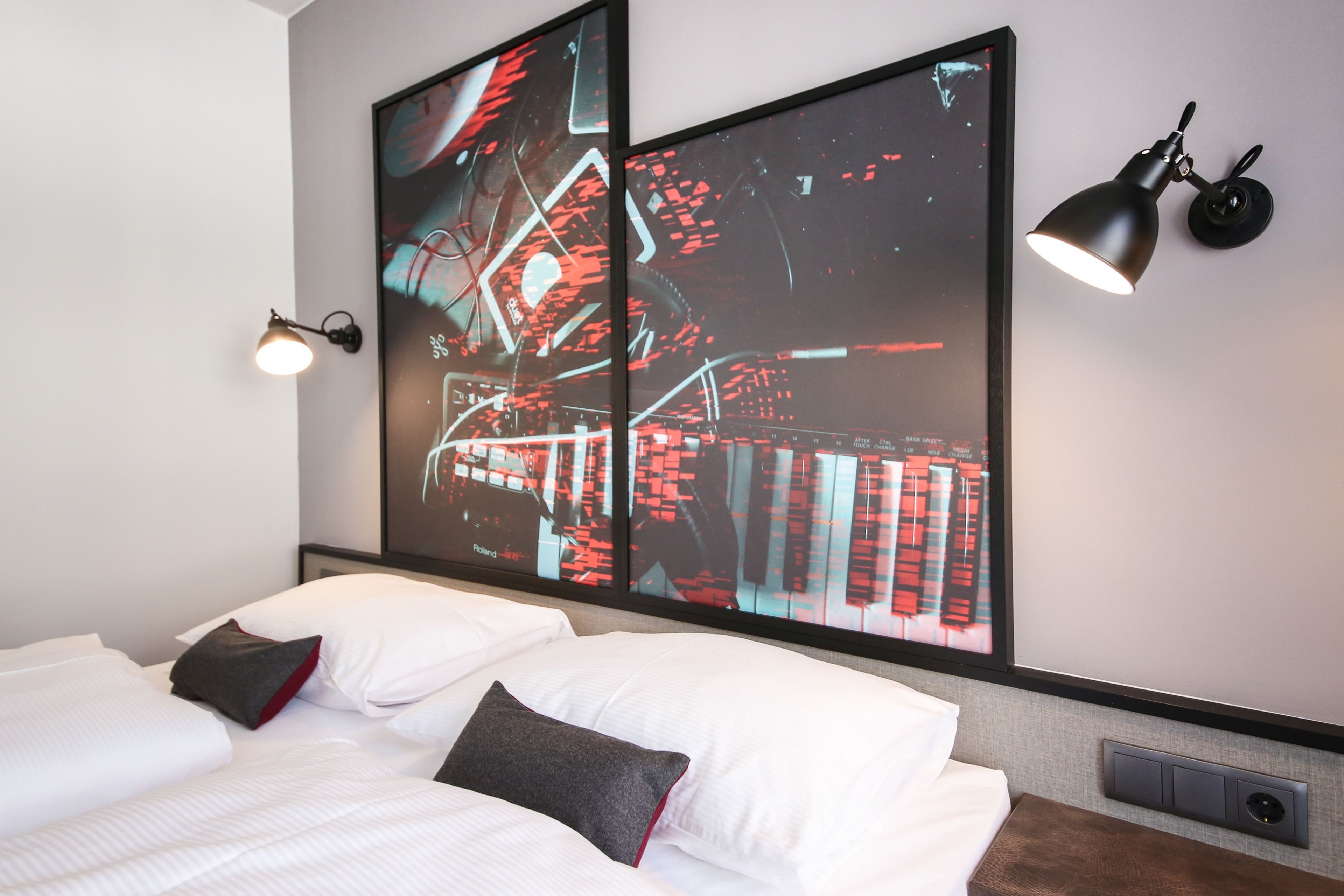 Un hotel moderno con una cama grande, un televisor empotrado que muestra un paisaje urbano, una lámpara de pared negra y un aire acondicionado integrado.
