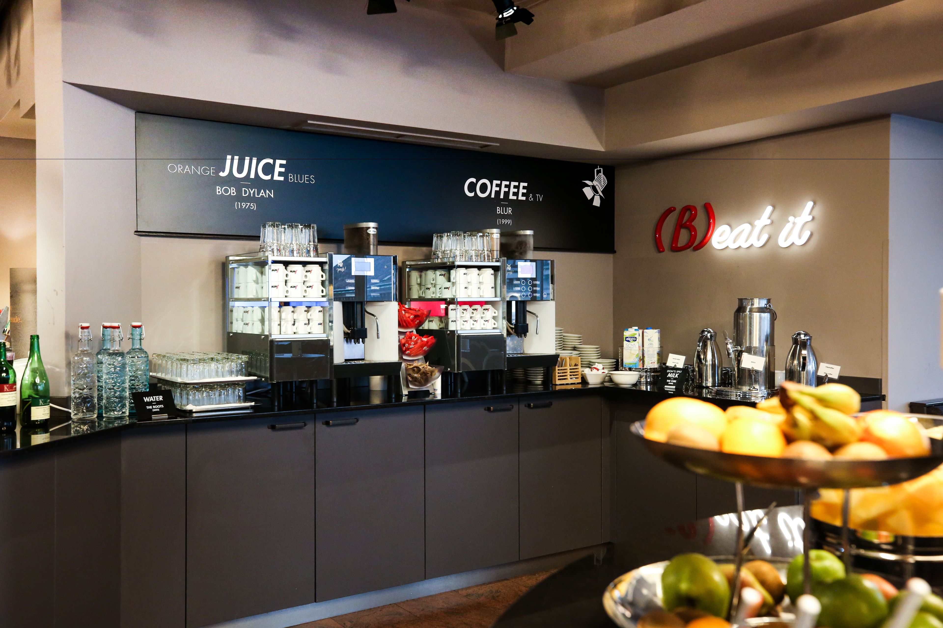 Un bar proposant des cafés, des jus de fruits et une variété de boissons, ainsi qu’un présentoir de fruits.
