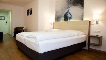 A hotel room with a large bed, bedside lamps, a headboard, a wall-mounted artwork, and a door leading to another room.