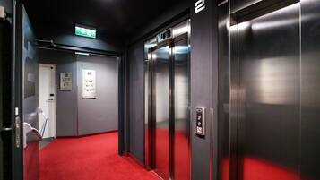 Un ascensor con piso alfombrado en rojo, señal de salida de emergencia y una puerta con el número 2.