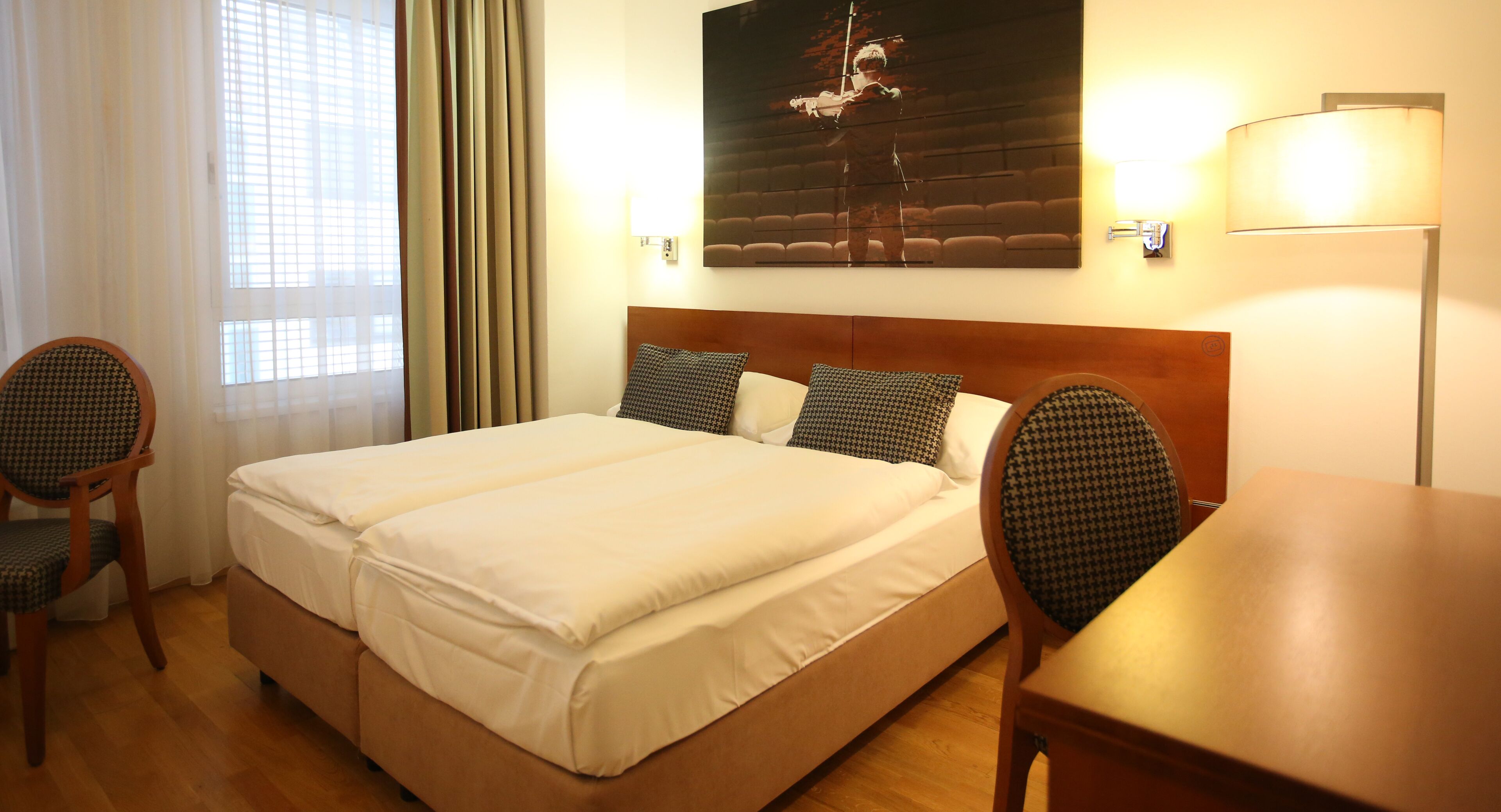 Una habitación de hotel con una cama grande, dos sillas, una mesa de madera y un cuadro en la pared.