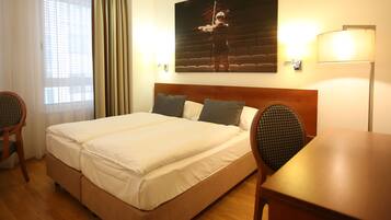 Una habitación de hotel con una cama grande, dos sillas, una mesa de madera y un cuadro en la pared.