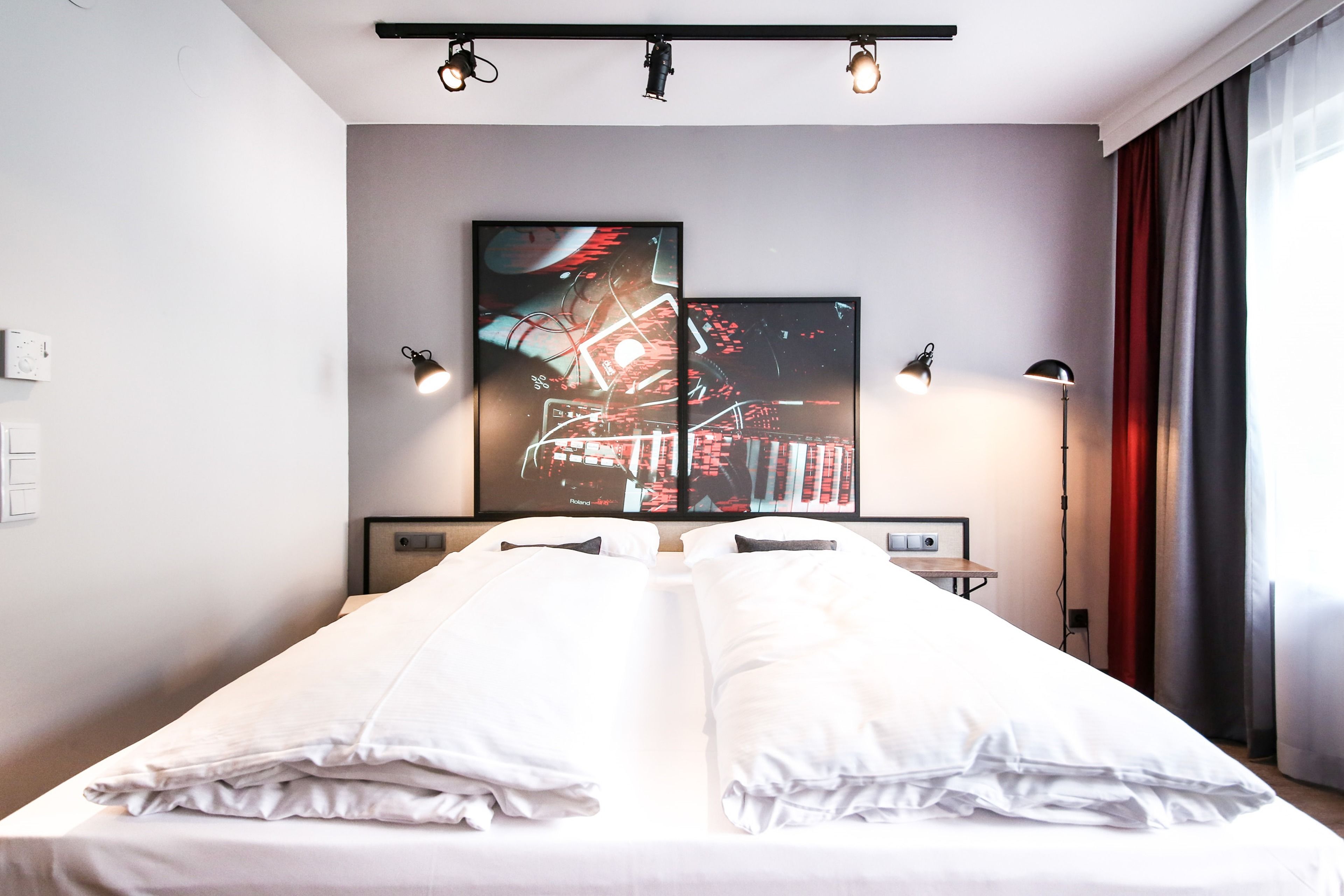Habitación de hotel moderna con una cama grande, dos lámparas fijadas a la pared y un cuadro abstracto de gran tamaño sobre la cama.
