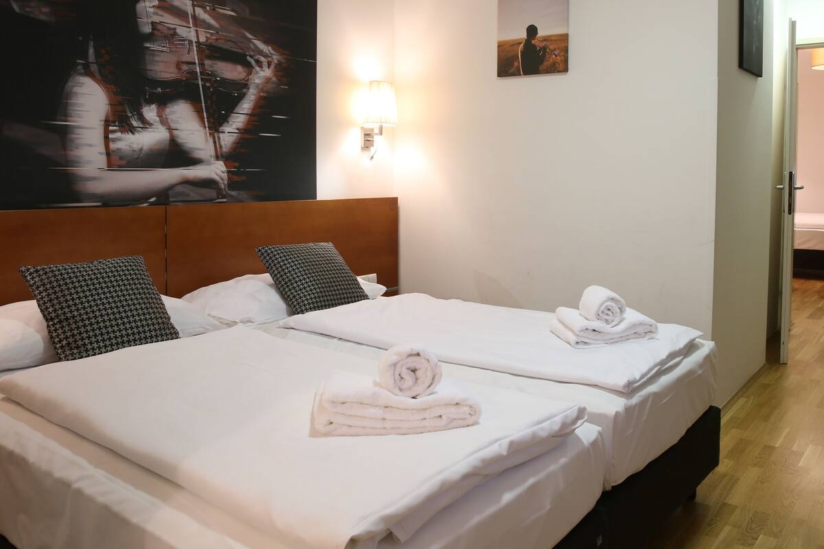 Une chambre d’hôtel avec deux lits, du linge de lit blanc et des serviettes. Il y a un tableau au mur et une lampe sur la table de chevet.