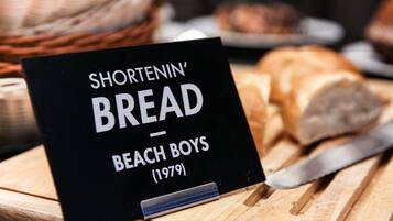 Un letrero con el texto 'Shortenin' Bread Beach Boys (1979)' sobre una superficie de madera, con pan y un cuchillo.