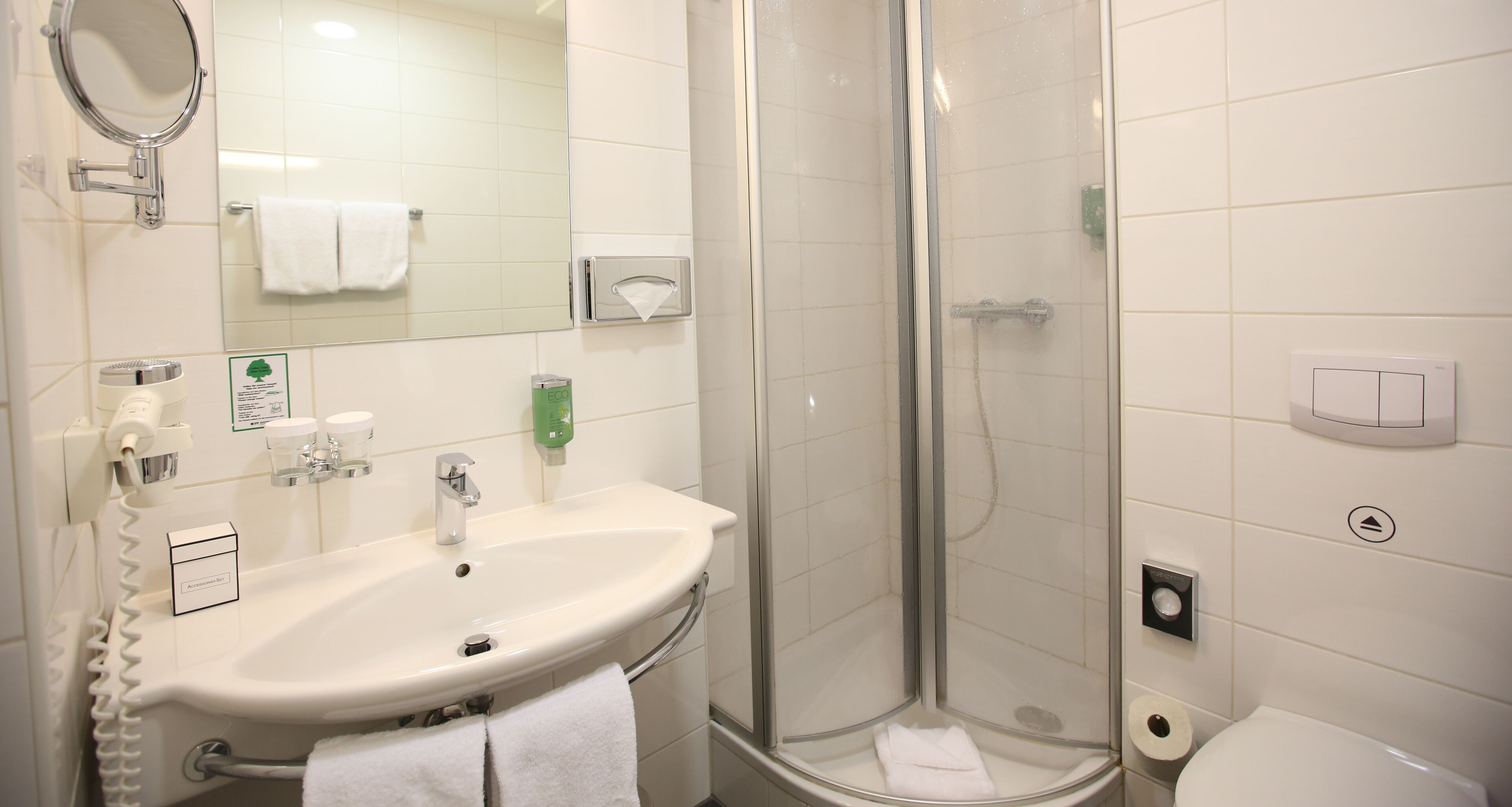 Un baño con lavamanos, espejo, toallero y ducha con mampara de vidrio.