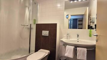 Un baño con ducha, inodoro, lavamanos y perchero para toallas.