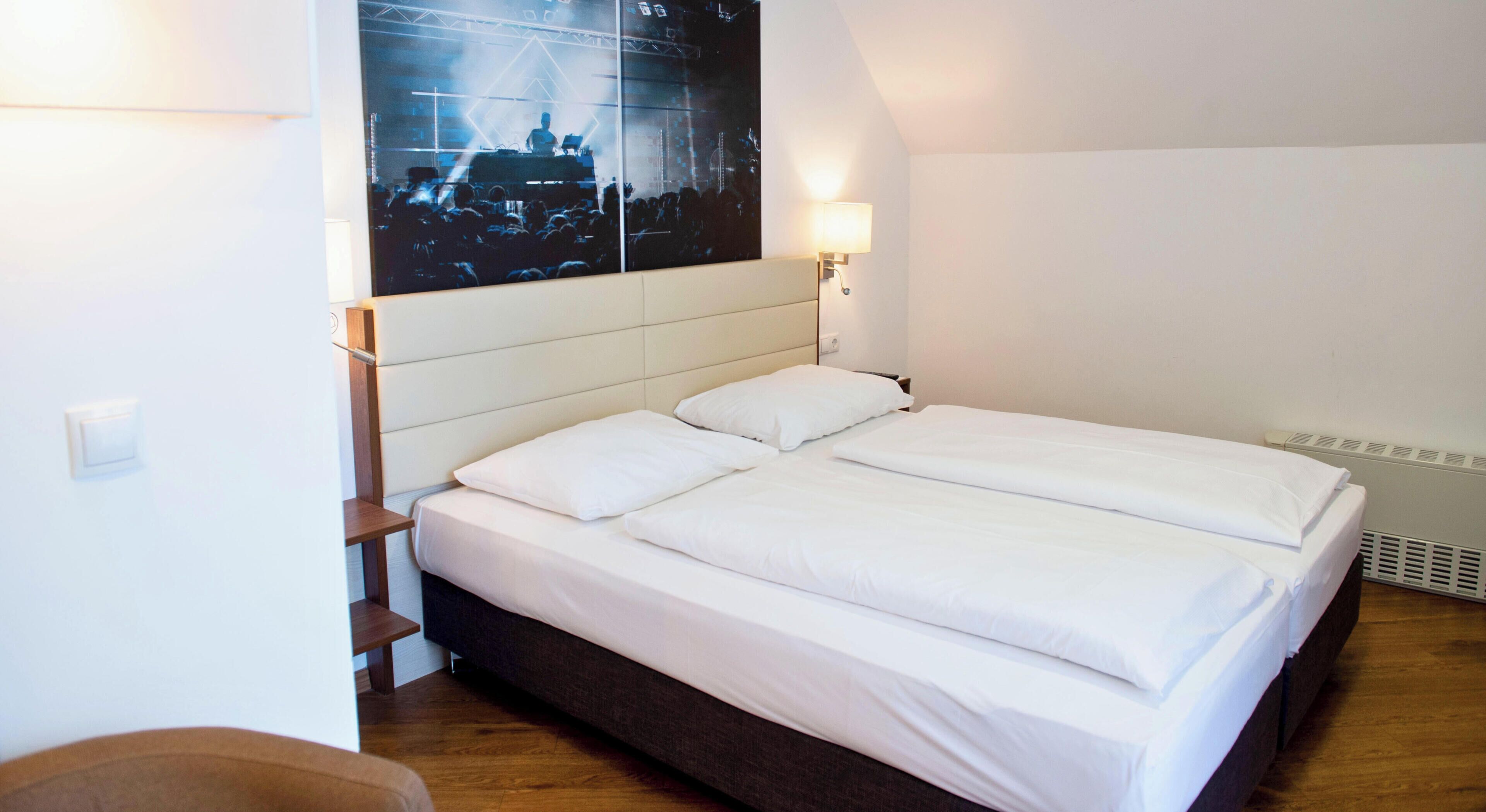 A bedroom with a bed, a nightstand, a wall-mounted lamp, and a poster on the wall.