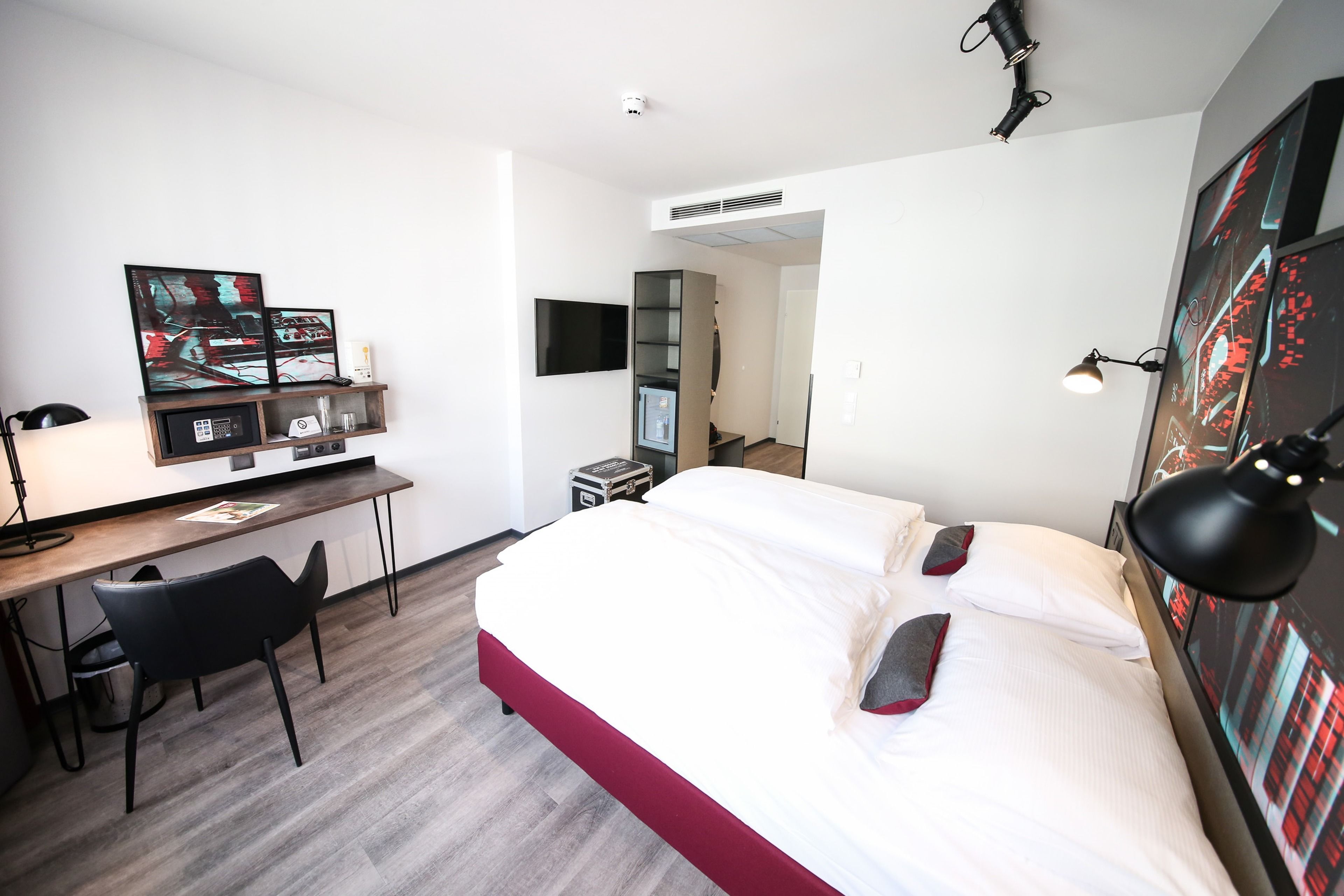 Une chambre d’hôtel équipée d’un lit, d’un bureau, d’une chaise et d’œuvres d’art accrochées aux murs.