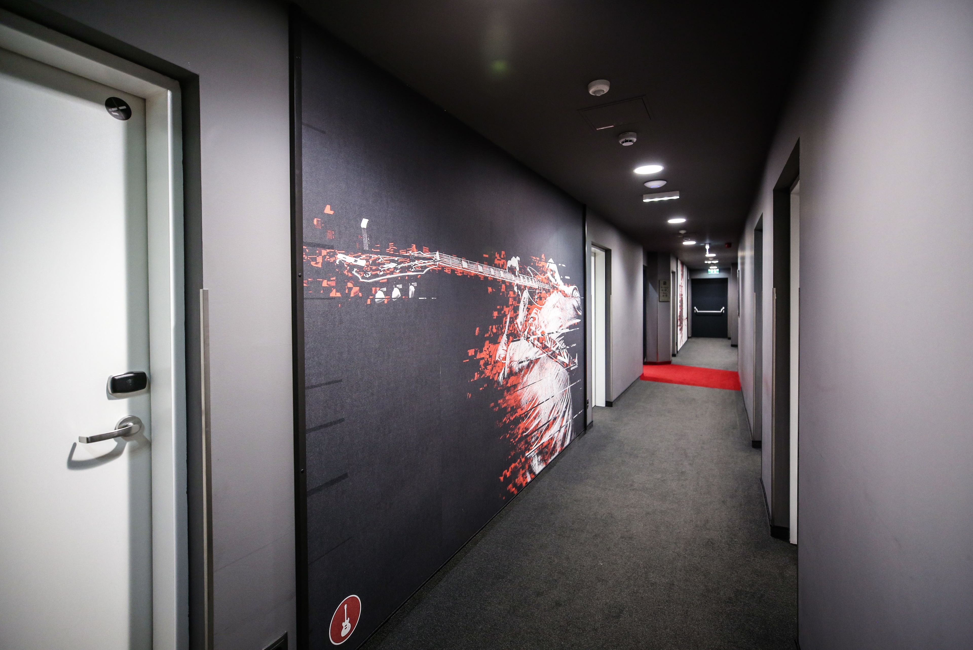 Un pasillo largo con alfombra roja y una pared con diseño abstracto en rojo y blanco.