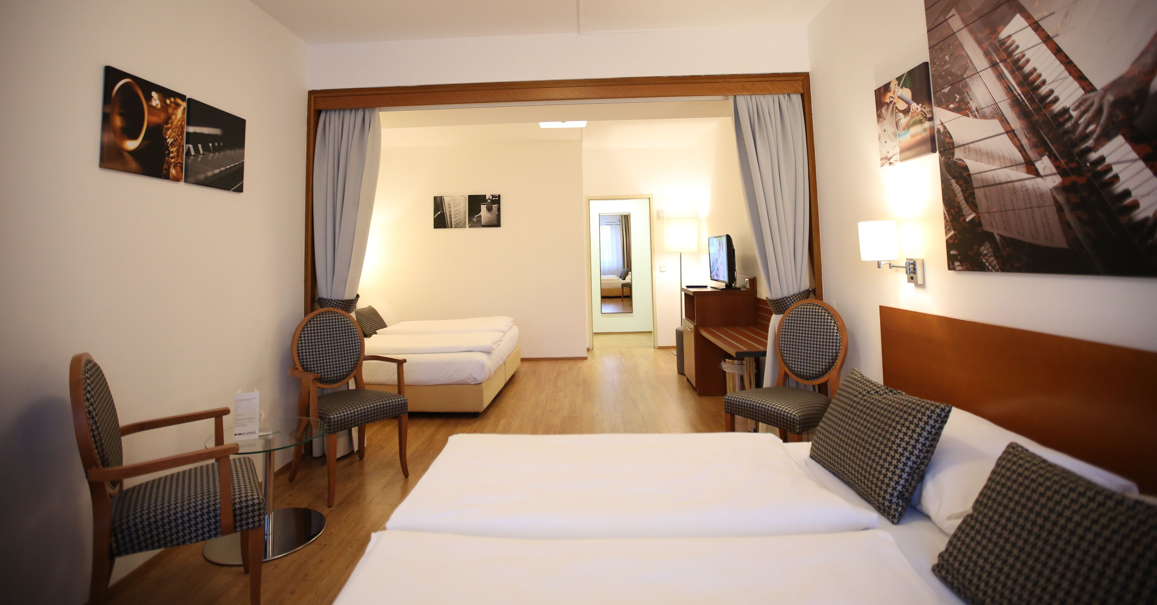 Habitación de hotel con una cama grande, dos sillas, un escritorio y una mesita. Se ve una puerta que conduce a otra habitación.